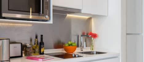 A modern kitchen with white cabinetry, a stainless steel microwave, a bowl of fruit, and a vase with a flower.