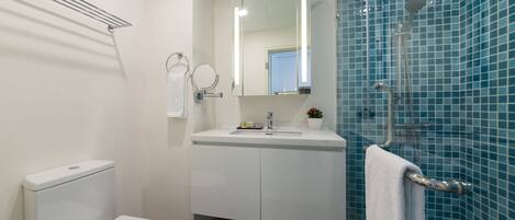 A modern bathroom with a toilet, sink, mirror, and shower.