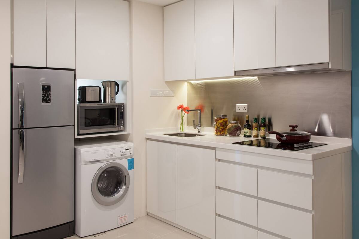 A modern kitchen with a refrigerator, microwave, oven, and washing machine.