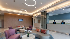 A modern lobby with a curved sofa, round coffee table, and purple armchairs. A reception desk with two staff members is visible. - Citadines DPulze Cyberjaya (Cyberjaya)
