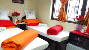 A hotel room with two beds, each with white linens and orange and red pillows. There are two vases with red roses on the nightstands, and a window with curtains. - Manila Hotel - Hostel (Kowloon)