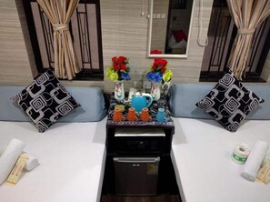 A room with a kitchenette, two patterned pillows, a table with a vase of flowers, and a window with curtains. - Manila Hotel - Hostel (Kowloon)