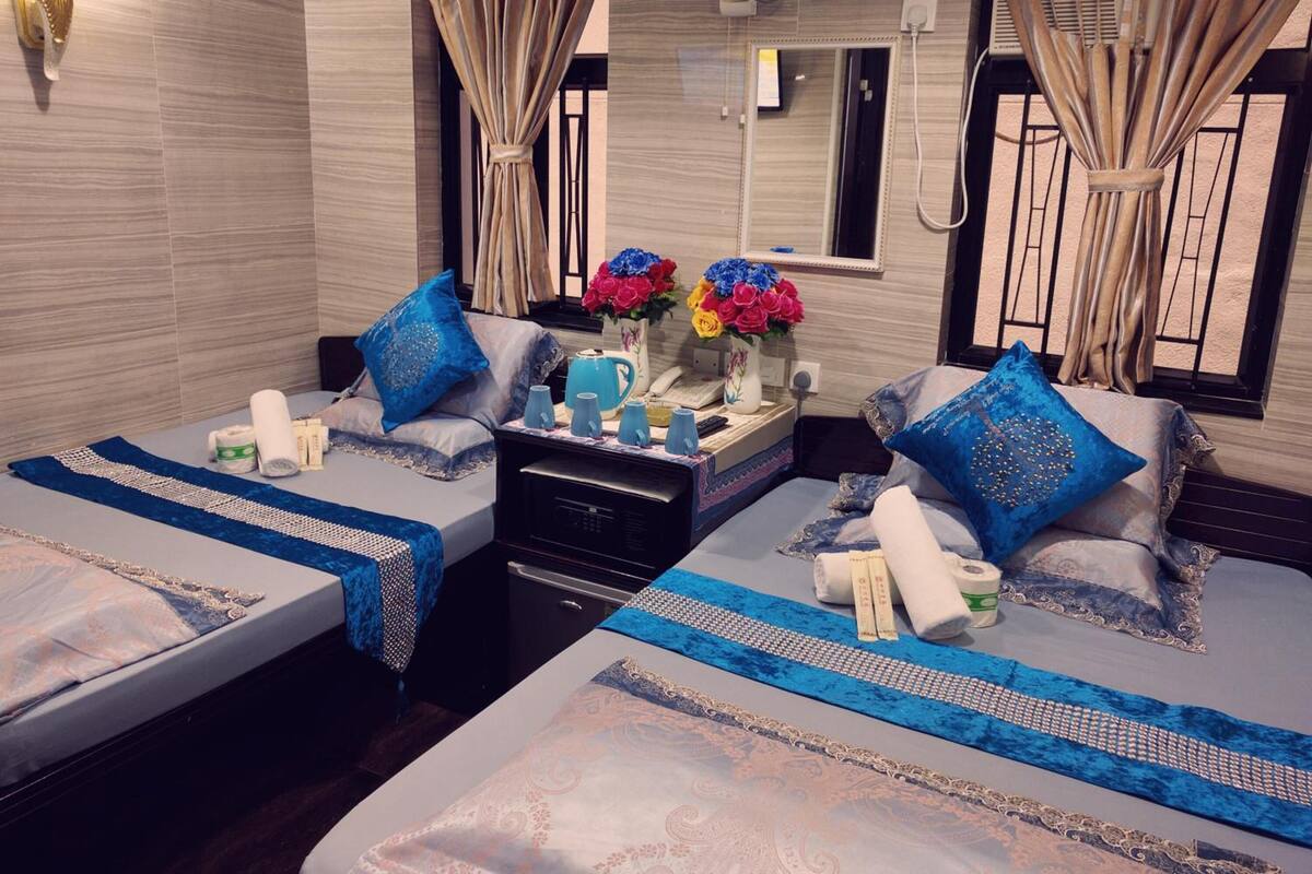 A hotel room with two beds, a small table with toiletries, a vase with flowers, and a fan.