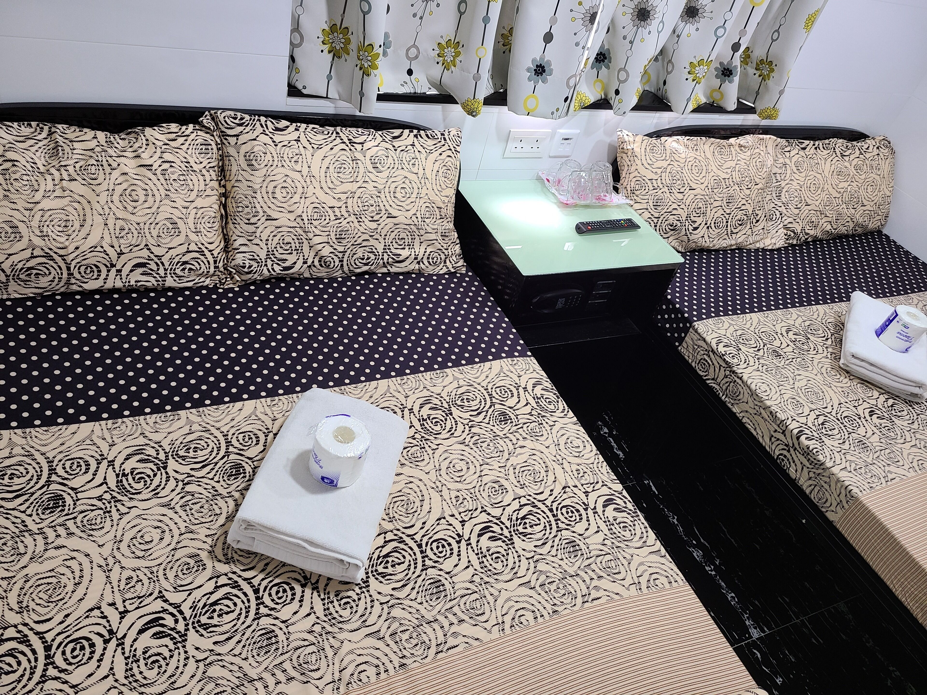 A room with a sofa set featuring a floral pattern, a small table with a remote control, and a rolled-up towel.