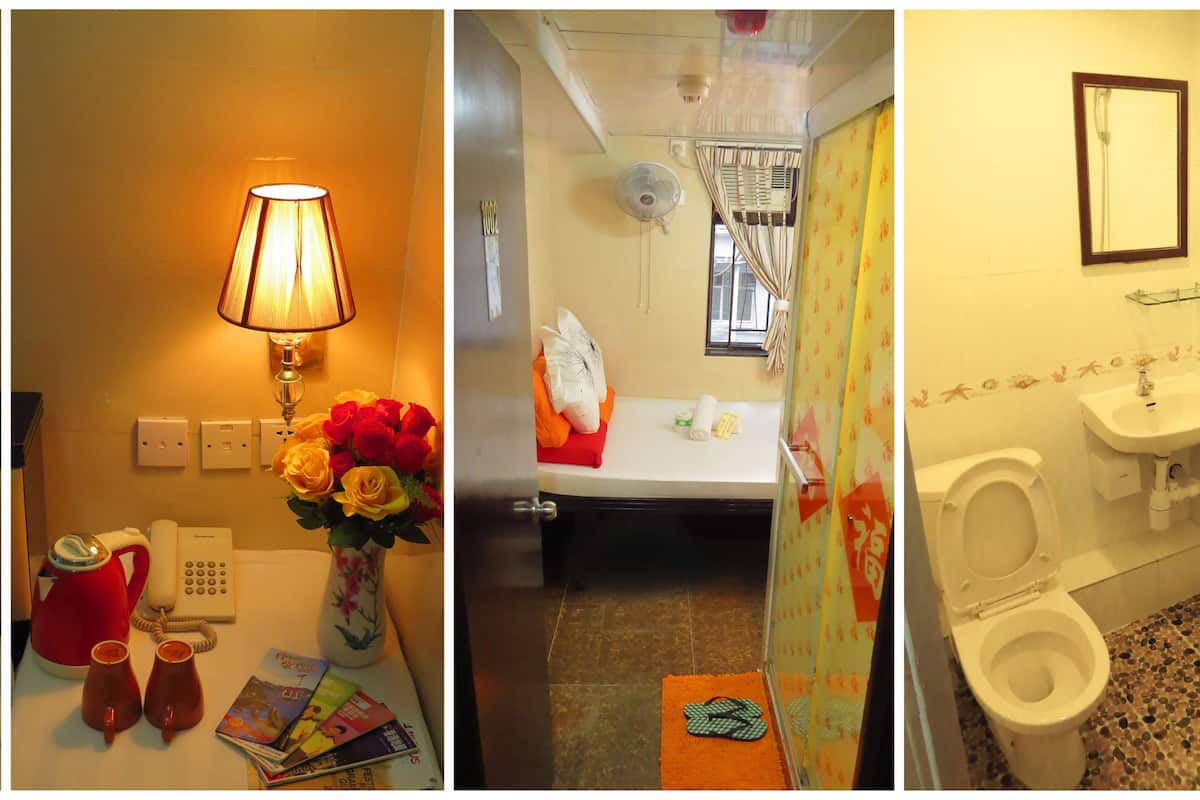 A hotel room with a bedside lamp, a vase of flowers, a red kettle, and a telephone on the nightstand.