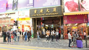 A busy street with a hotel entrance, Chungking Mansions, and various shops. - Hong Kong Budget Hostel (Kowloon)