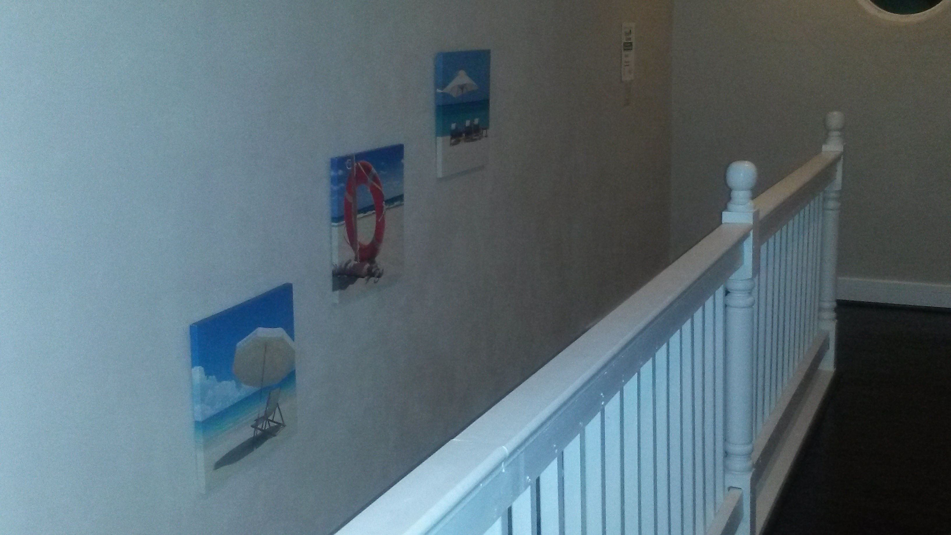 En hall med ett vitt räcke, en ljusströmbrytare och tre inramade tavlor på väggen.