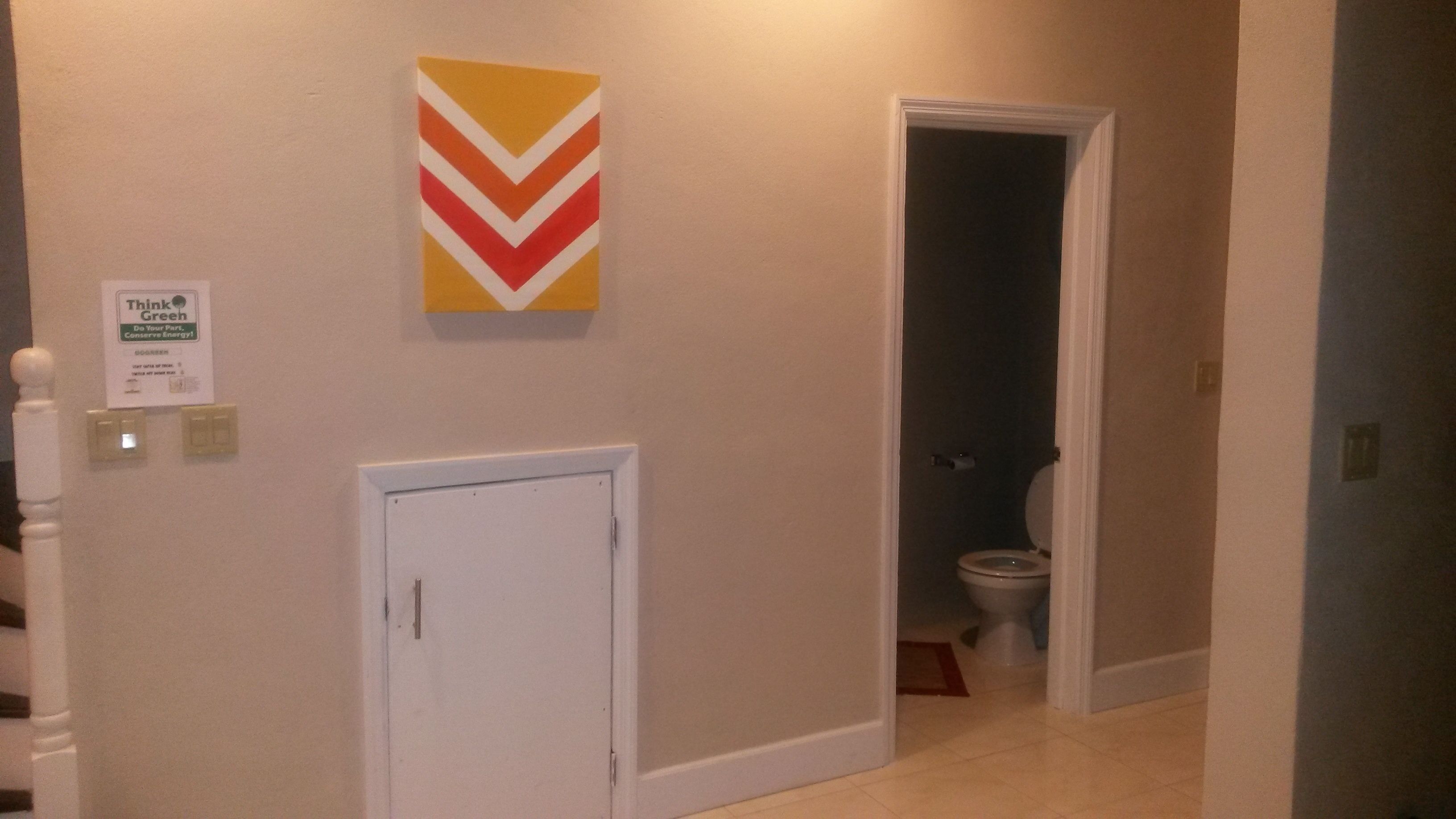 A hallway with a chevron-patterned wall decoration, a closed door, and a toilet visible in the adjacent room.