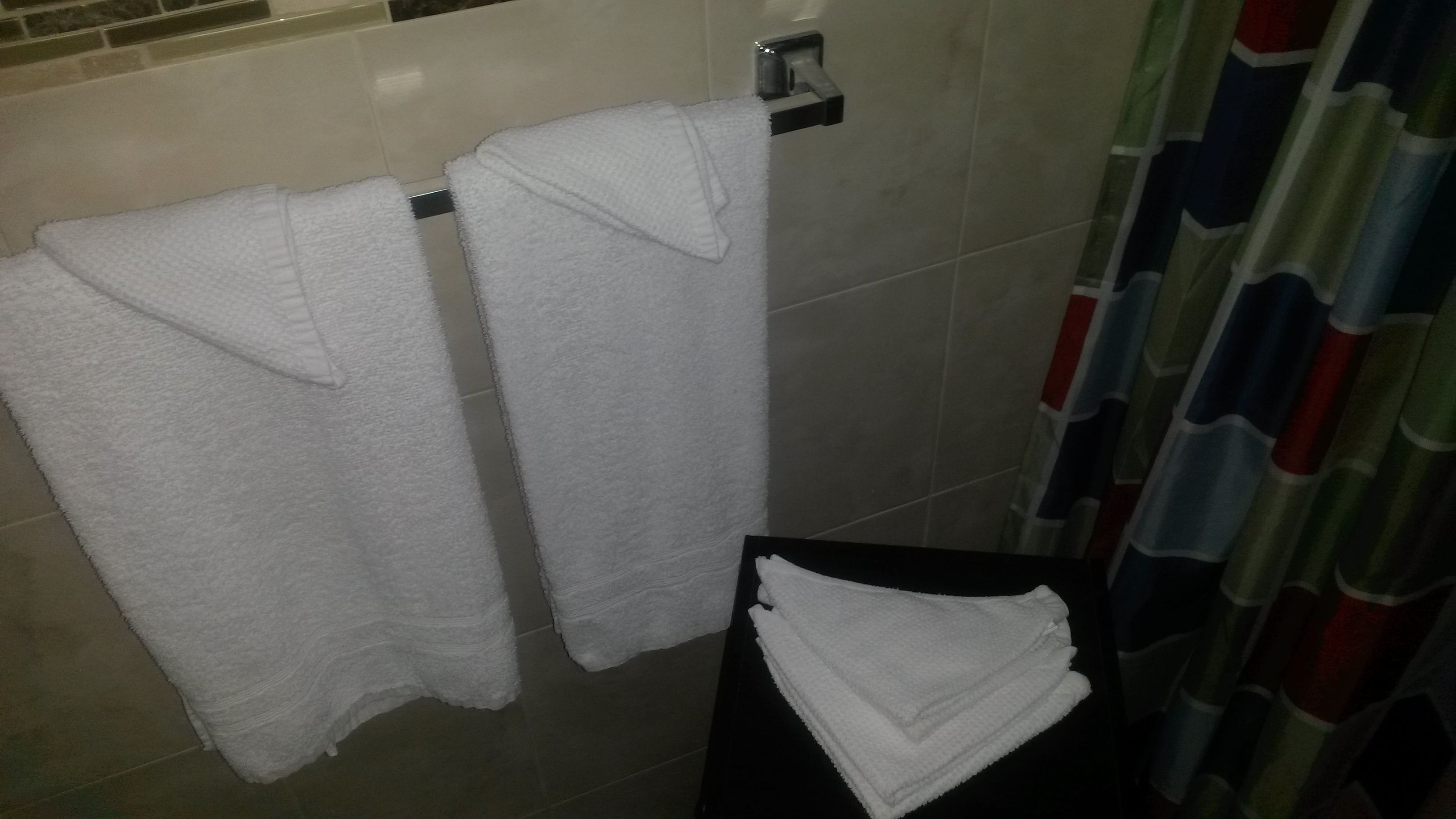 A bathroom with two white towels hanging on a rack and a stack of towels on a table.
