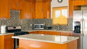 A kitchen with wooden cabinets, a granite countertop, a microwave, a coffee maker, and a stainless steel refrigerator. - Taste of Paradise (Nassau)