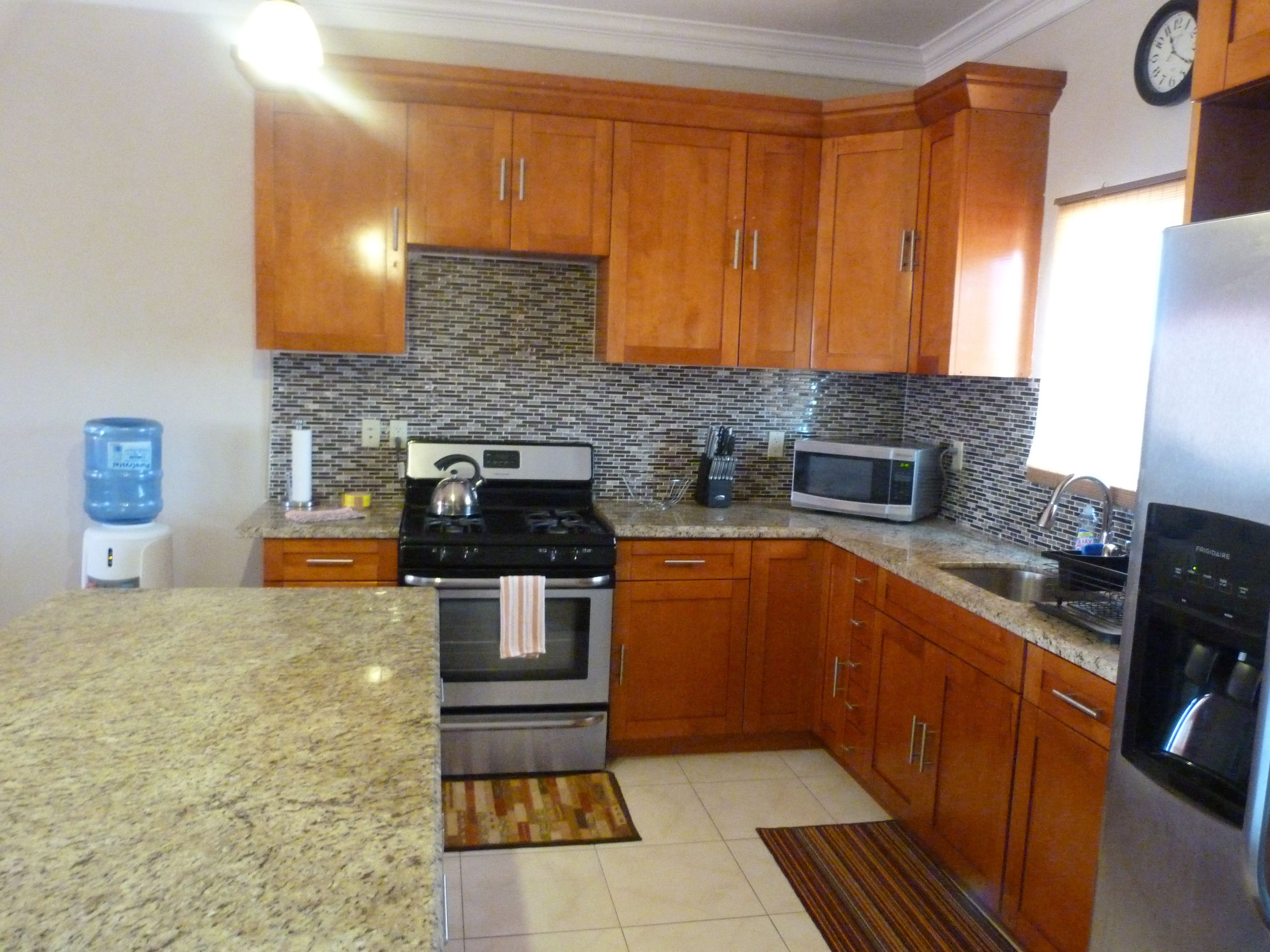 Una cocina con armarios de madera, encimera de granito, estufa, microondas y refrigerador.