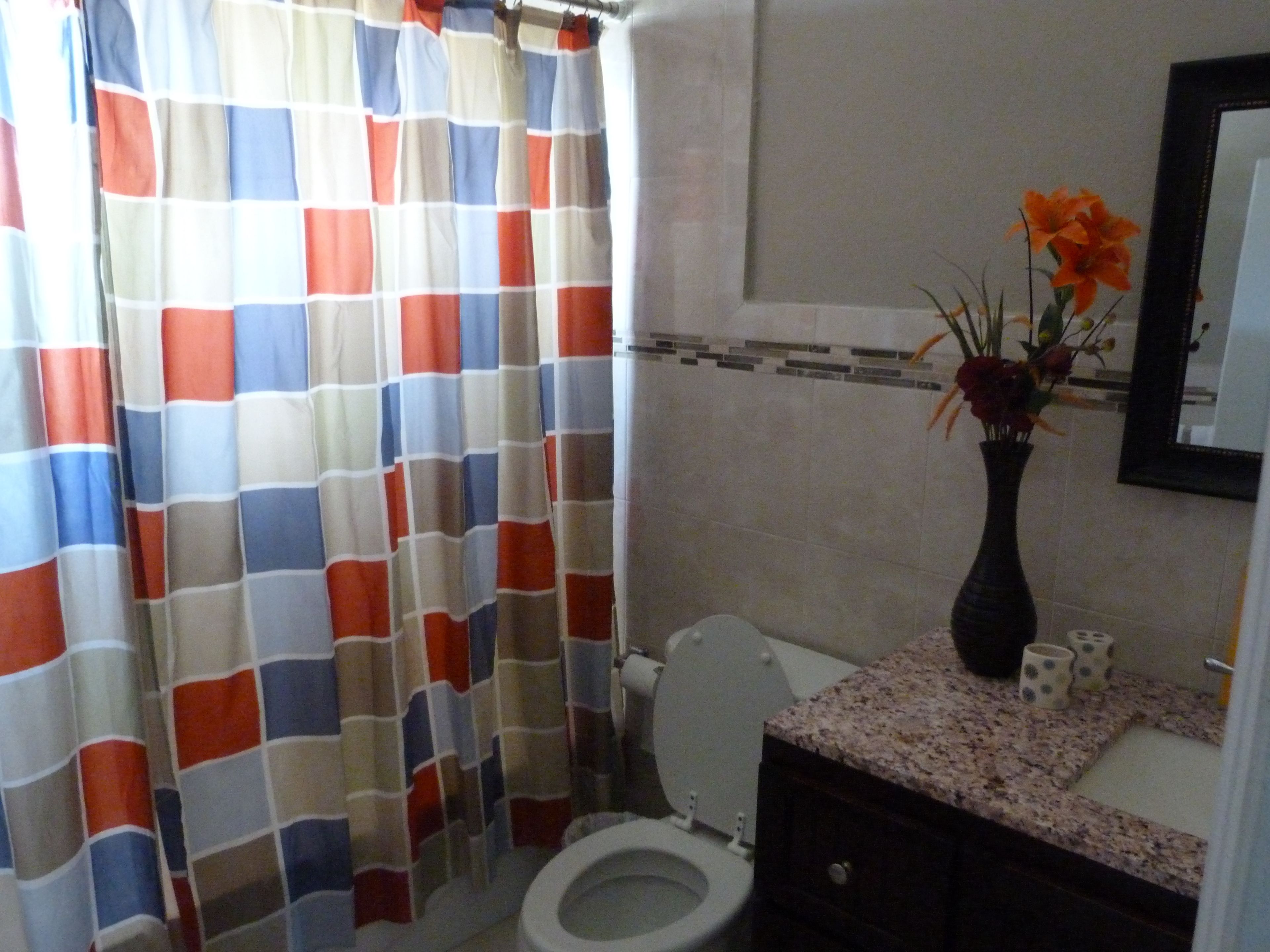 A bathroom with a toilet, a sink with a vase of flowers, and a shower curtain with a checkered pattern.