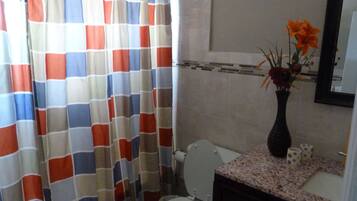 A bathroom with a toilet, a sink with a vase of flowers, and a shower curtain with a checkered pattern.