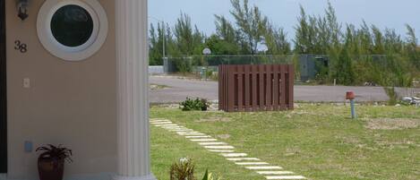 A building entrance with a white column, a potted plant, and a paved pathway leading to a gate.
