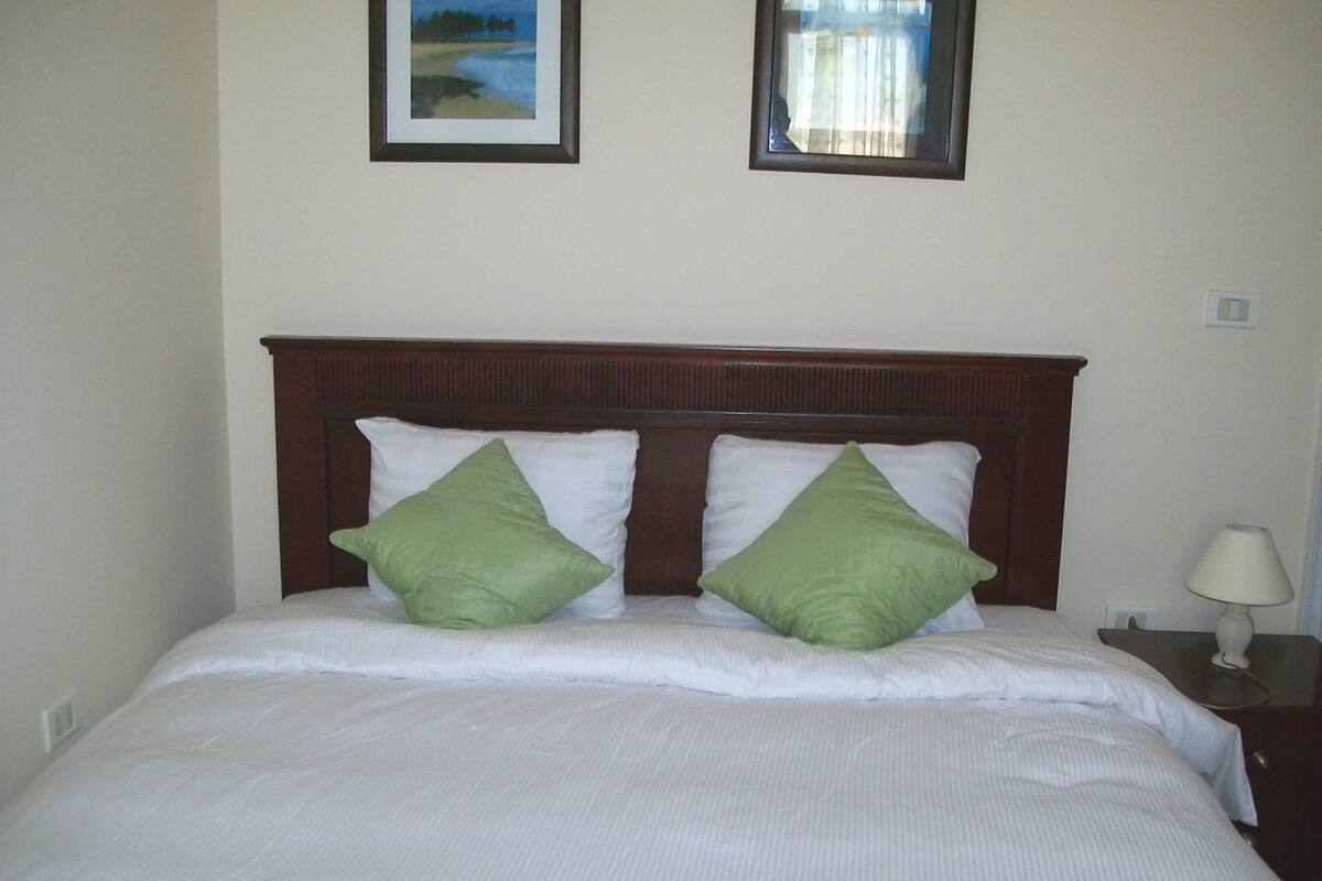 A neatly made bed with two green pillows and a wooden headboard.
