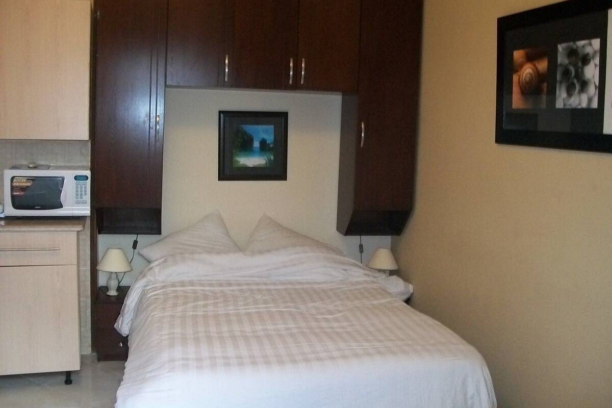A hotel room with a bed, a nightstand with a lamp, a microwave, and a framed picture on the wall.