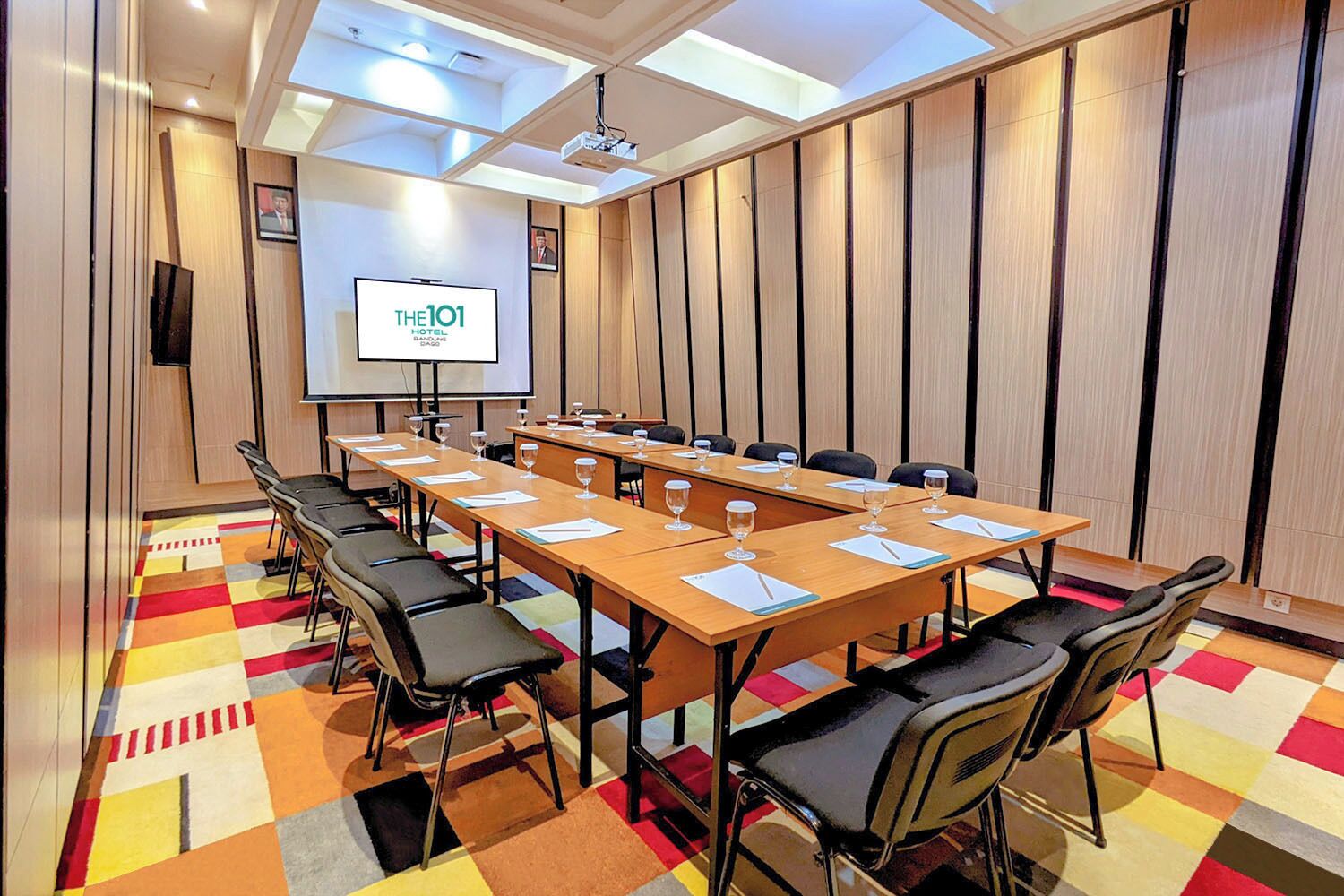 A conference room with a long table, chairs, a projector screen, and a colorful carpet.