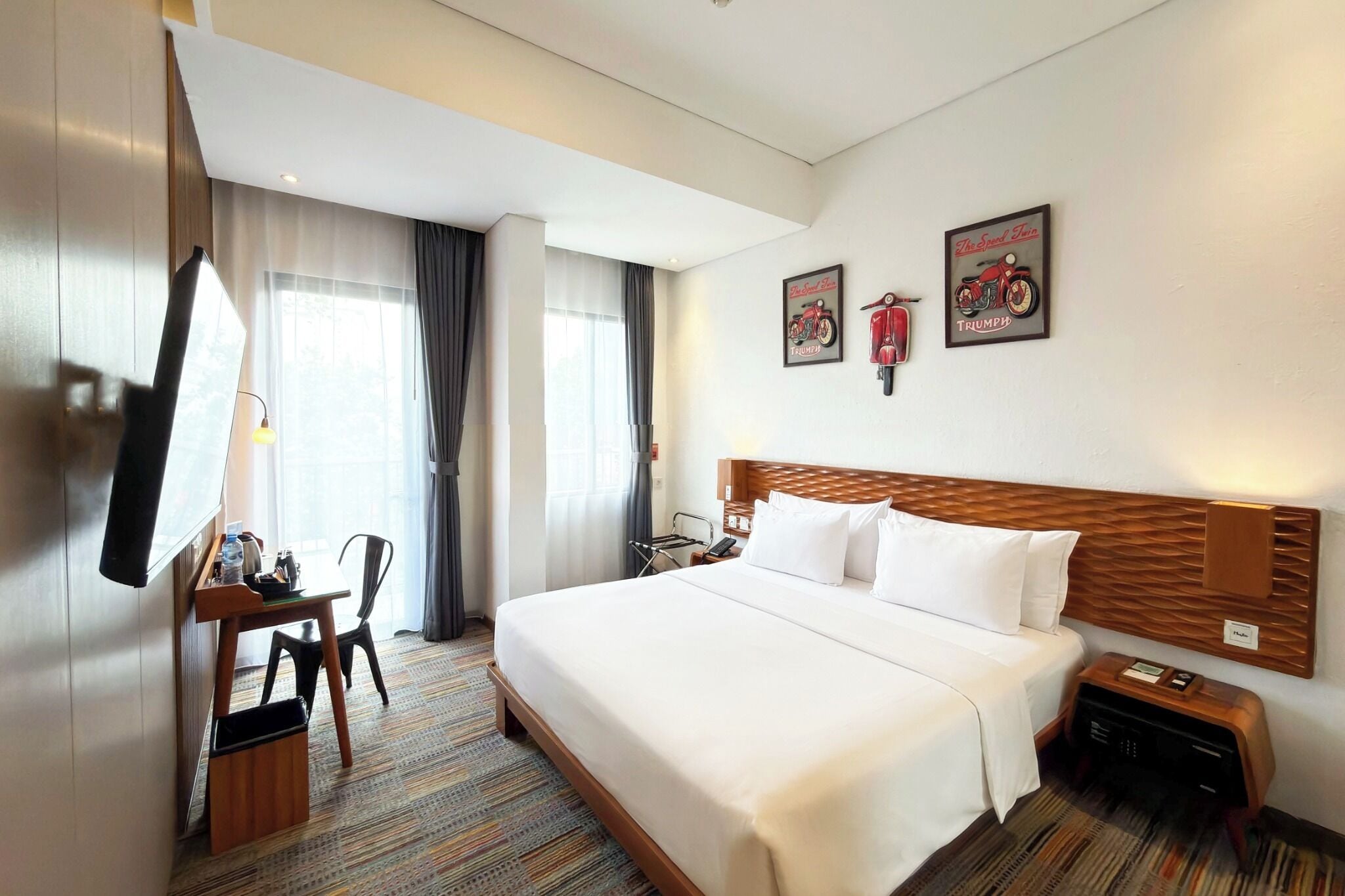 A hotel room with a large bed, a desk with a chair, a TV, and a window with curtains.