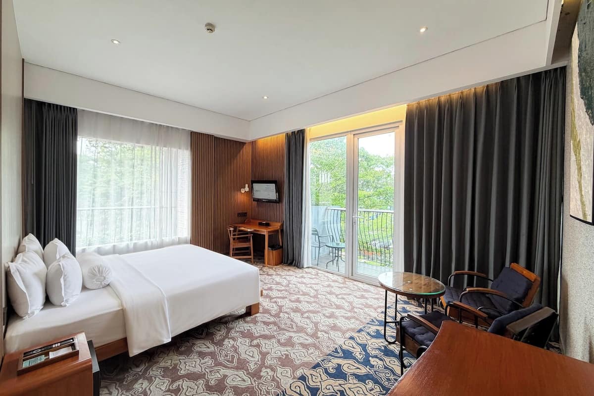 Quarto de hotel com cama, escrivaninha, cadeira, mesa pequena e varanda com vista.
