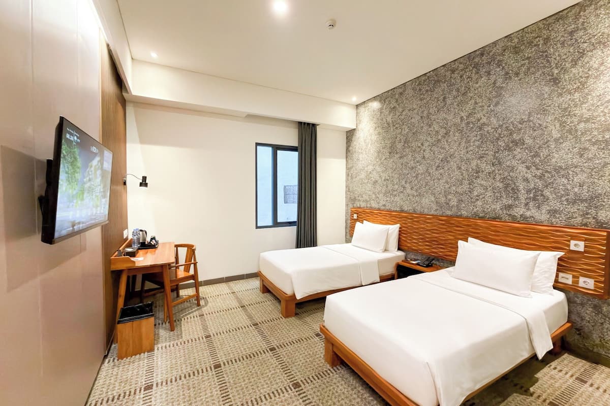 Quarto de hotel com duas camas, uma escrivaninha, uma cadeira, uma televisão e uma janela.