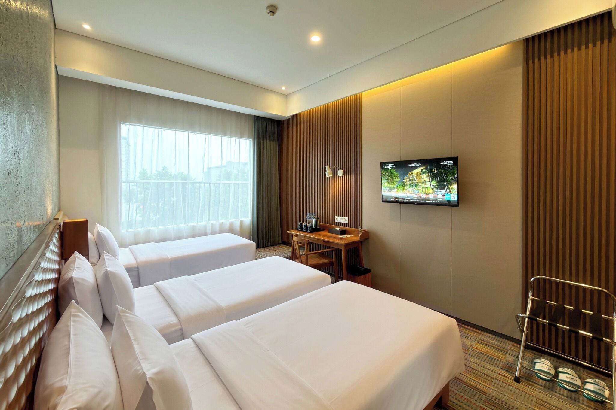 Ein Hotelzimmer mit zwei Betten, einem Schreibtisch, einem Fernseher und einem fensterbepflanzten Fenster.
