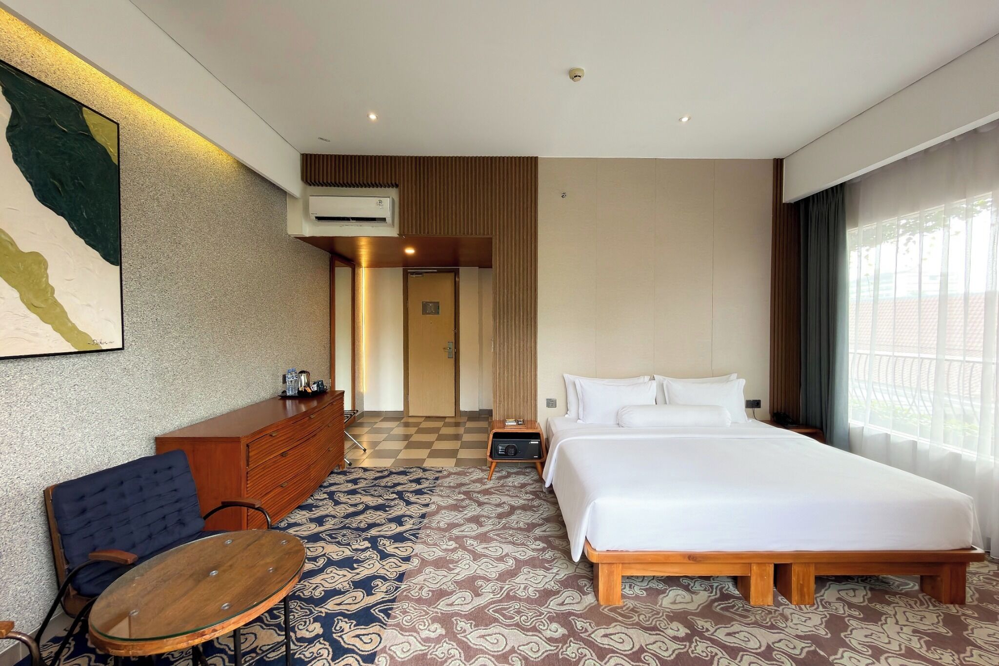 A hotel room with a large bed, a small table, a sofa, a dresser, and a painting on the wall.