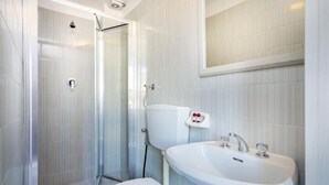 Un baño moderno con ducha de vidrio, inodoro blanco y lavamanos con espejo.