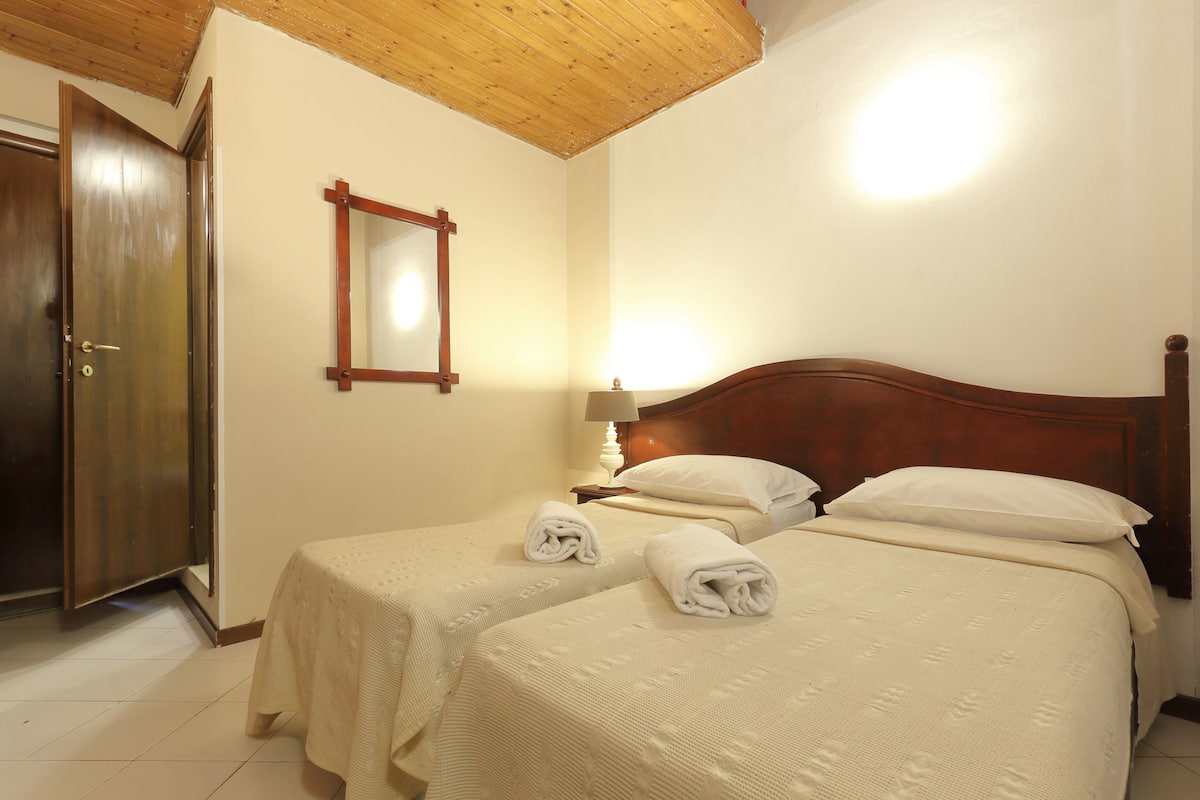 A hotel room with two beds, a wooden door, a mirror, and a lamp.