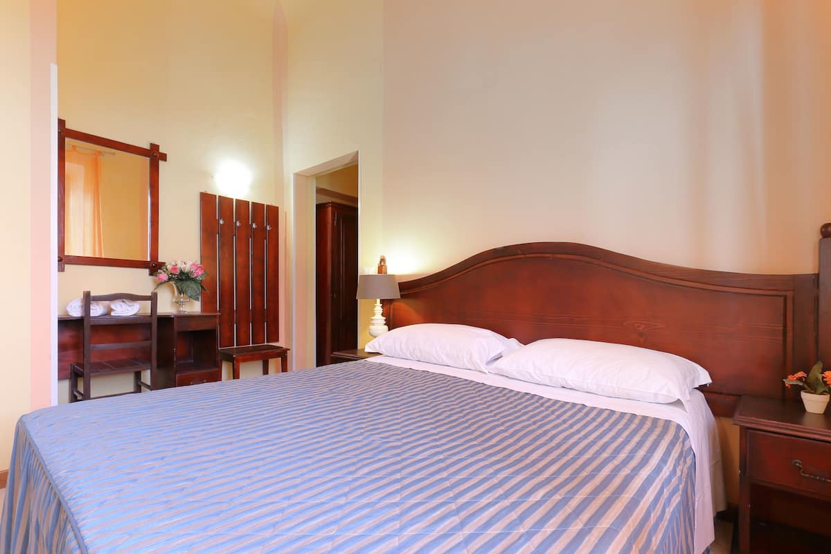 A neatly made bed with a striped bedspread, a wooden headboard, and a nightstand with a lamp and a small potted plant.