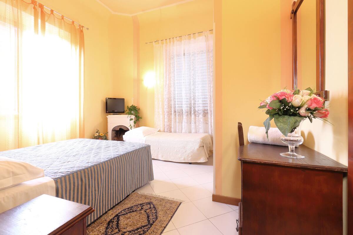 A bedroom with a bed, bedside table, and a dresser with a vase of flowers.