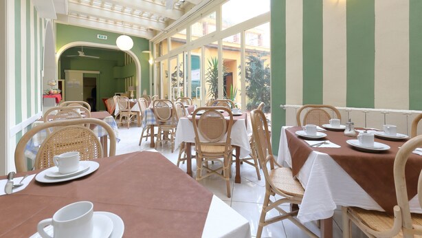 Un restaurante con mesas preparadas para comer, sillas de mimbre y vistas al exterior.