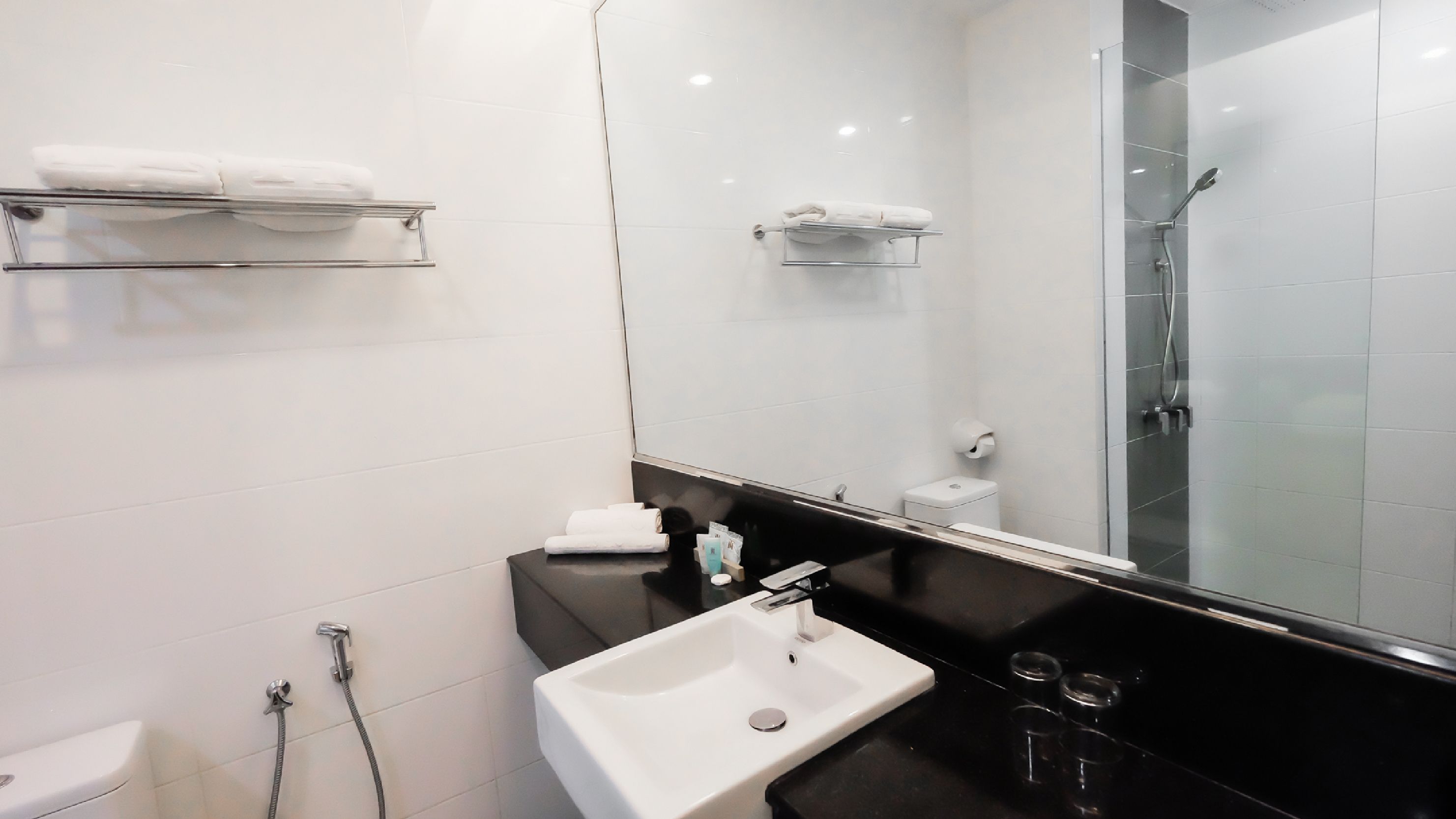 Une salle de bain moderne avec un lavabo blanc, une douche en verre et des serviettes blanches rangées sur des étagères.