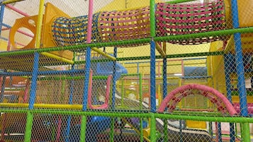 A multi-level play structure with netted climbing areas and slides, enclosed by a safety fence.