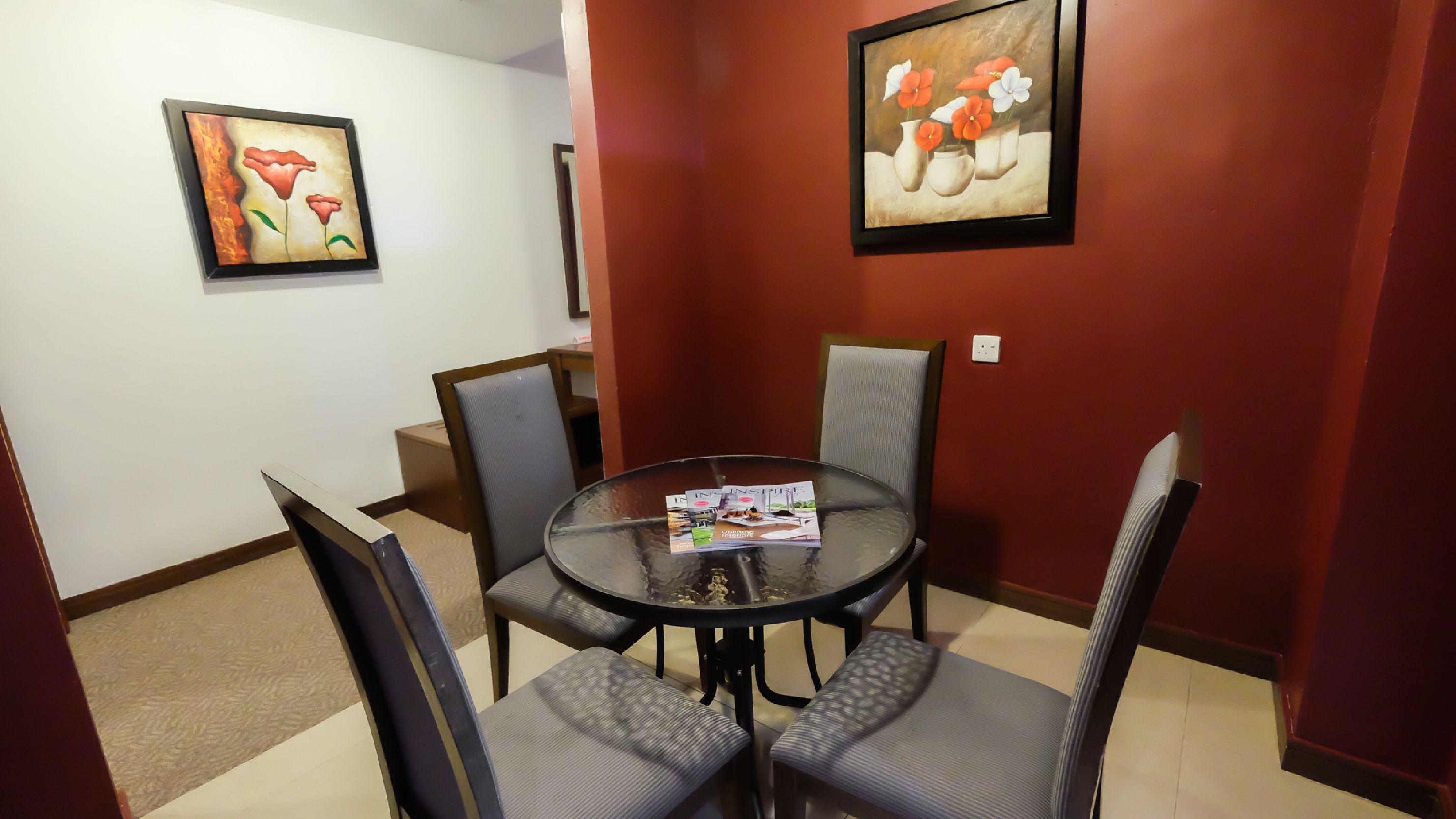 A dining area with a round table and four chairs, a magazine on the table, and two paintings on the walls.