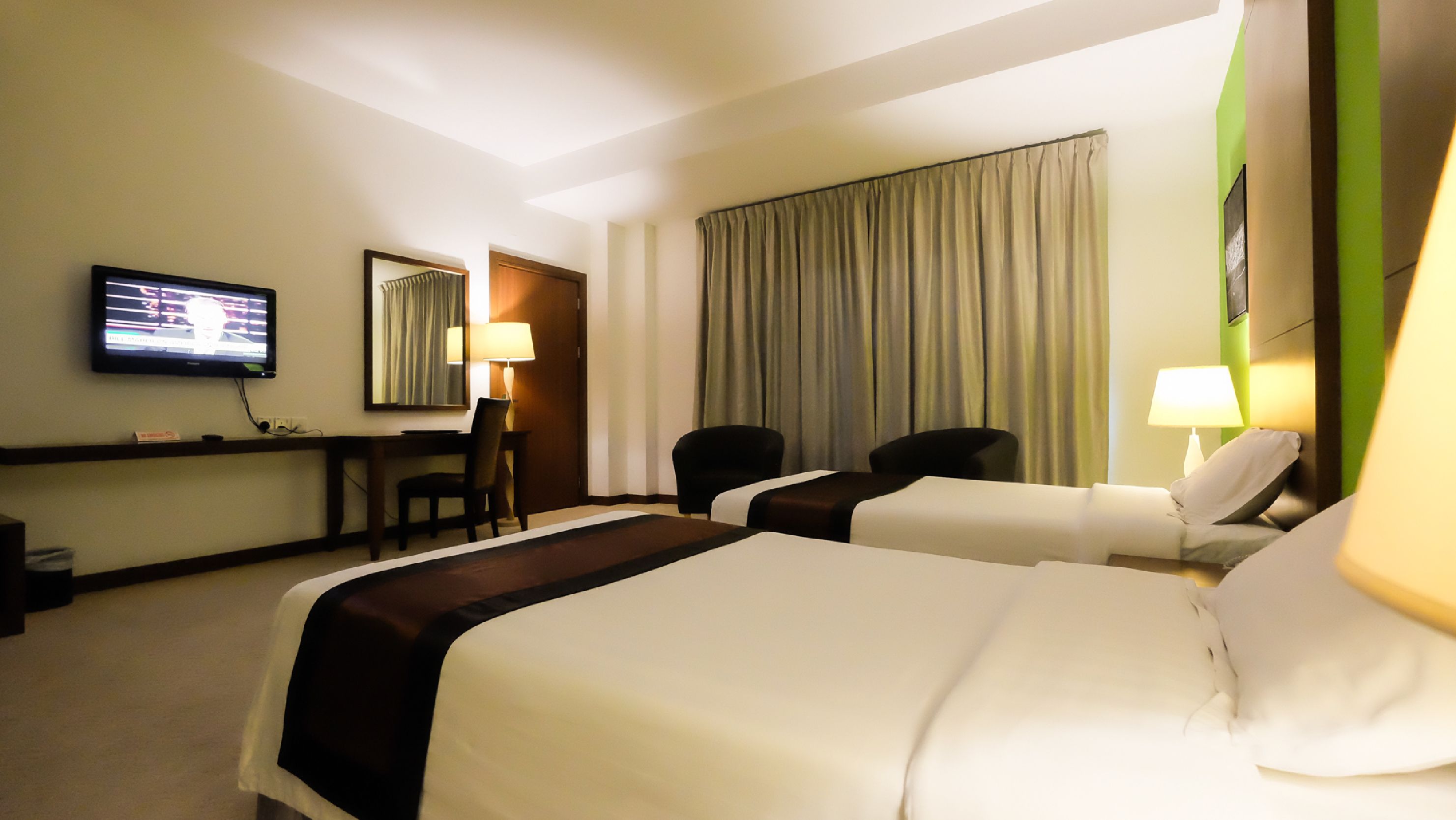 A hotel room with two beds, a desk, a chair, a television, and a window with curtains.