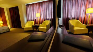 A hotel room with a bed, two yellow armchairs, a small table, a TV, and a window with curtains.