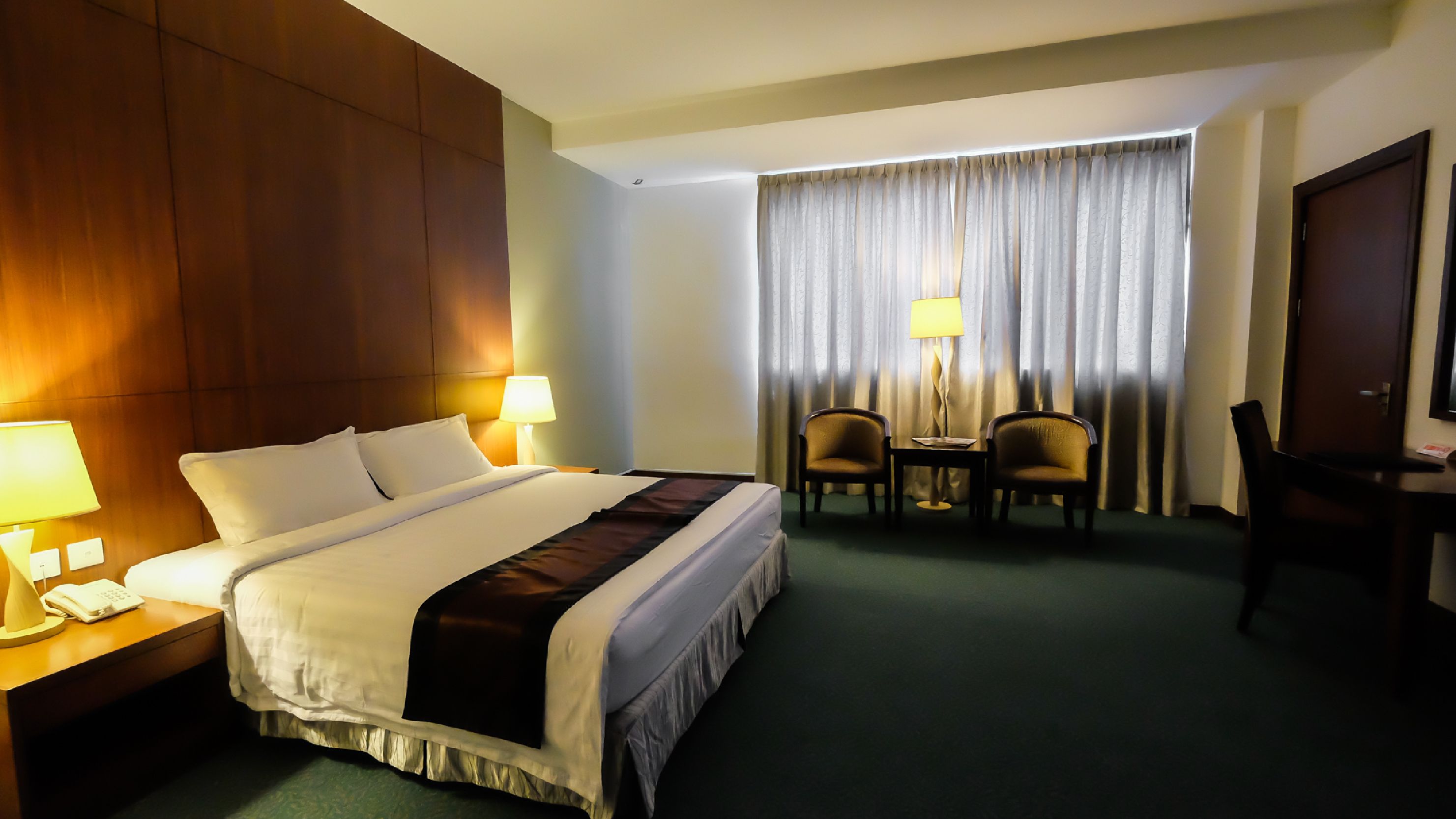 A hotel room with a bed, two chairs, a desk, a lamp, and a television.