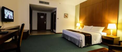 A hotel room with a bed, bedside lamps, a desk with a computer, a chair, and a television on the wall.