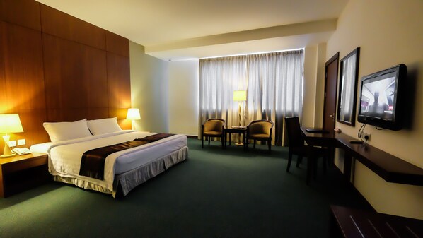 A hotel room with a large bed, two chairs, a desk, a television, and a window with curtains.
