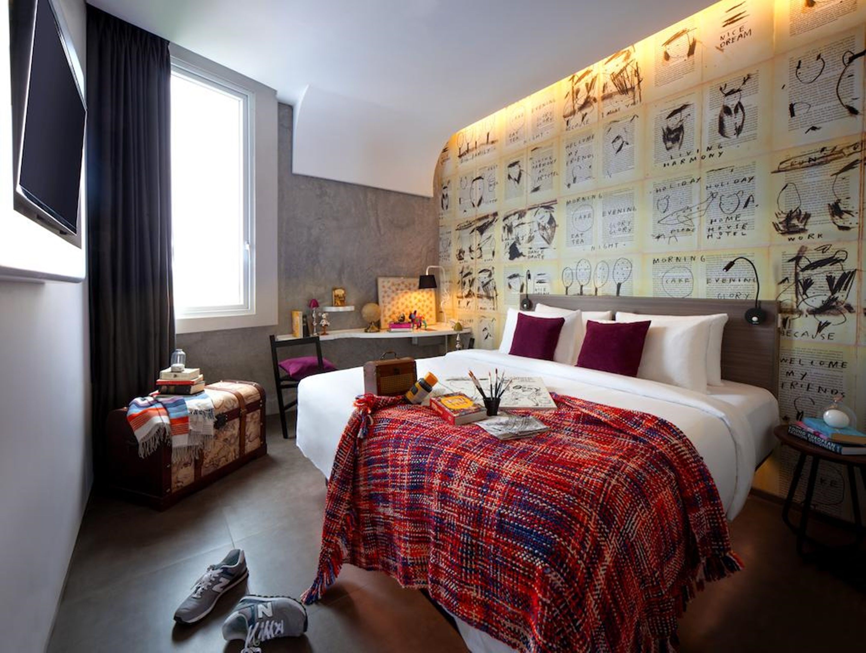 Een hotelkamer met een groot bed, een bureau en een muur vol schetsen.