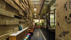 A long corridor with wooden benches and tables, a glass wall with plants, and hanging lights. - ARTOTEL Thamrin Jakarta (Jakarta)