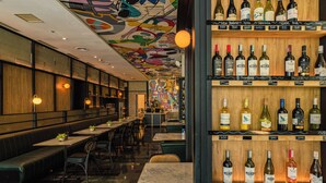 A restaurant with a bar area featuring a variety of wine bottles on shelves, booths, and tables with chairs. - ARTOTEL Thamrin Jakarta (Jakarta)