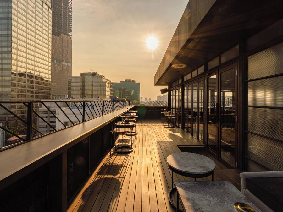 Una terraza en la azotea con vistas al horizonte urbano, que cuenta con cubierta de madera, asientos exteriores y ventanas grandes.
