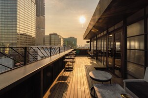 Una terraza en la azotea con vistas al horizonte urbano, que cuenta con cubierta de madera, asientos exteriores y ventanas grandes.