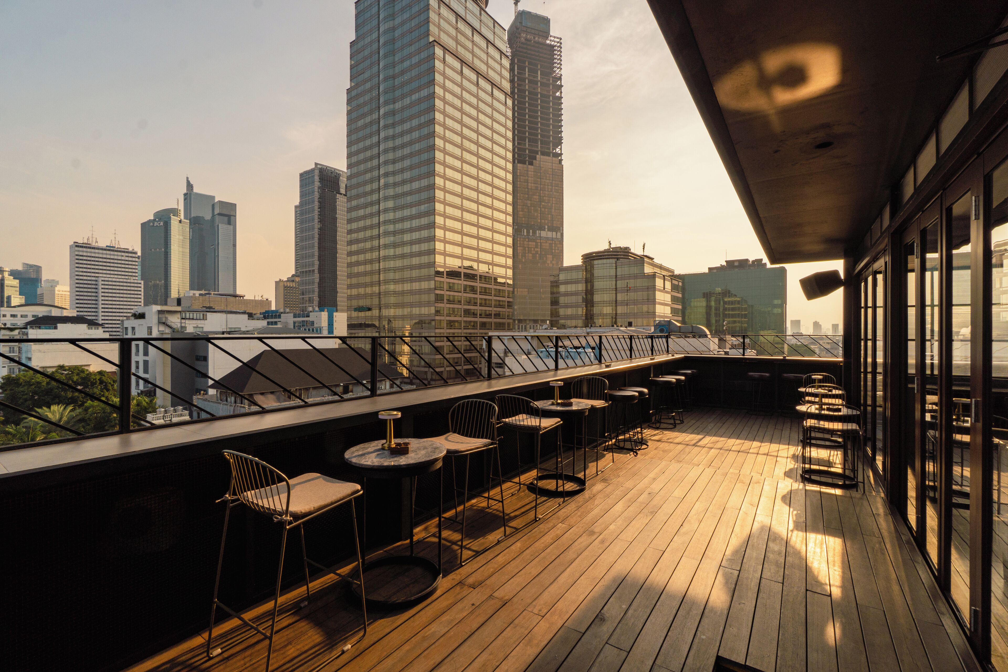 Un bar en la azotea con mesas al aire libre, con vistas a un horizonte urbano de edificios modernos.