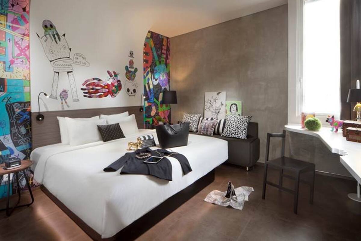 A modern hotel room with a large bed, bedside tables, a desk, and a window.