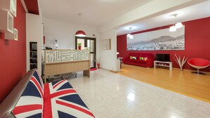 A reception area with a red and white color scheme, a reception desk, a large cityscape mural, a red sofa, and a wooden floor. - Hotel Las Palmas Urban Center (Las Palmas de Gran Canaria)