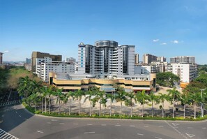 Stunning hotel with a curved corner and balconies, set amidst a beautifully landscaped area with palm trees.