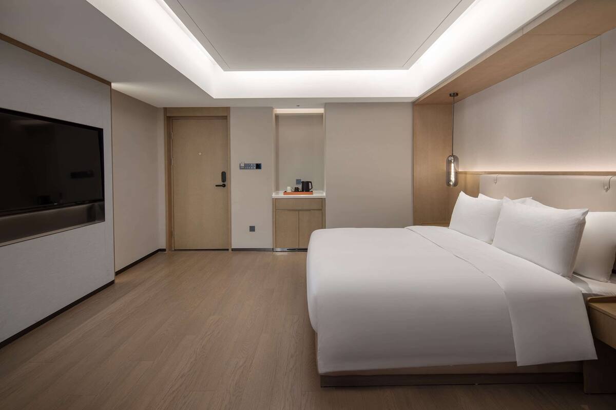 Een moderne hotelkamer met een groot bed, een flatscreen televisie, een kleine kitchenette en een plafondlamp.