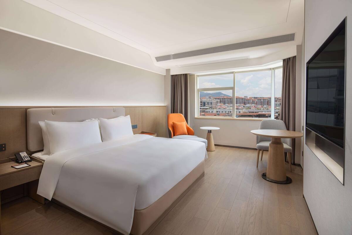 Een hotelkamer met een groot bed, een bureau met telefoon, een kleine tafel, een oranje fauteuil en een televisie.